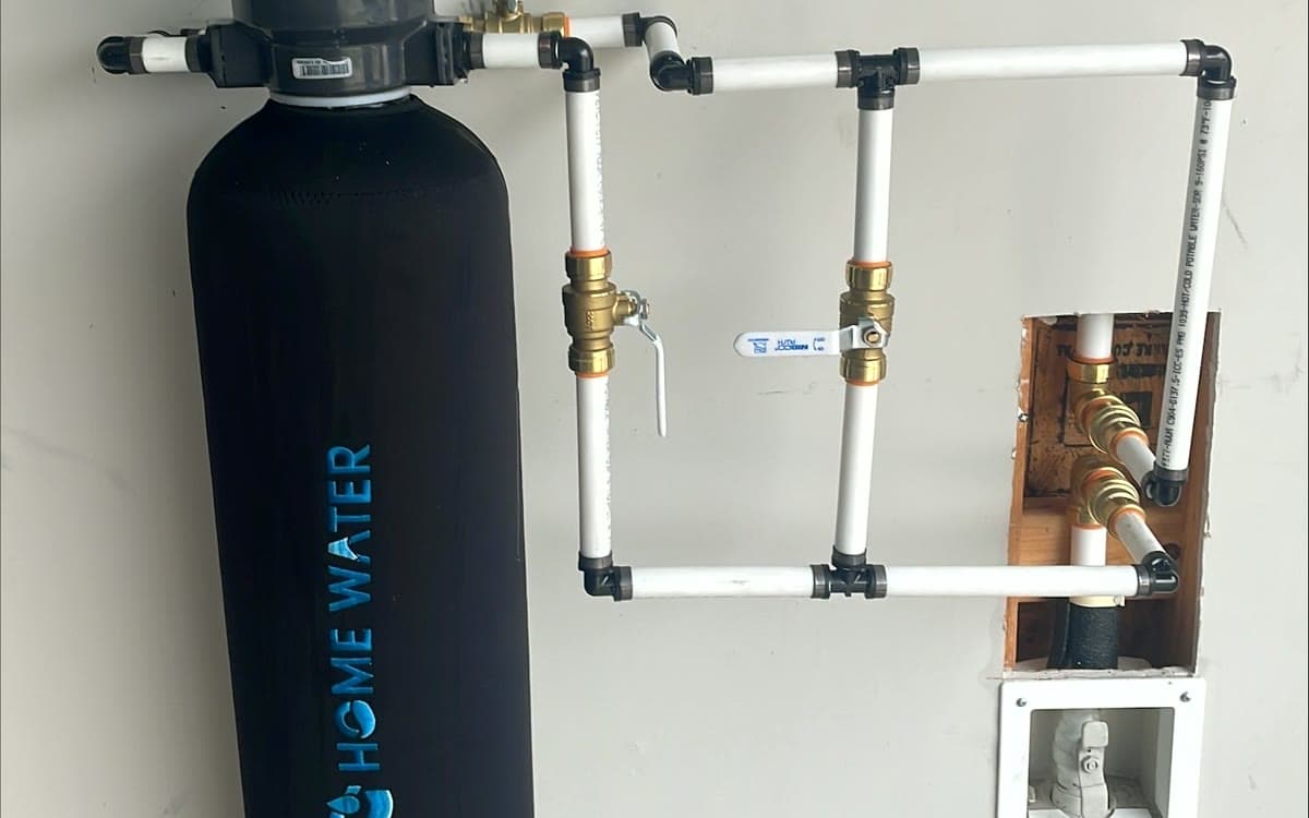 A HomeWater whole-home filter installed against a garage wall with its plumbing tie-in.